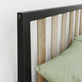 Close-up of modern bed headboard with black metal frame and light oak vertical slats next to green linen pillow on a white wall, minimalist bedroom decor