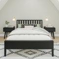 Black wooden bed frame in a minimalist Scandinavian bedroom with white bedding, matching black nightstands and a geometric patterned rug