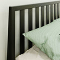 Close-up of modern black metal vertical-slat headboard with light green linen pillow and beige bedding in a minimalist bedroom setting