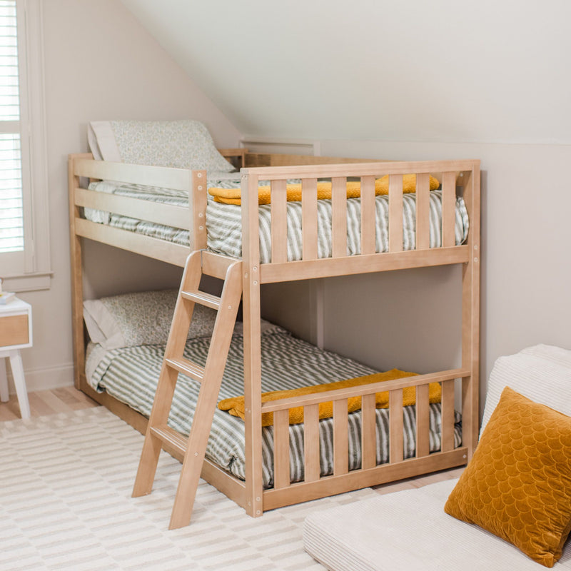 Wooden bunk bed with striped bedding in a cozy attic bedroom featuring a soft yellow pillow on a white couch.