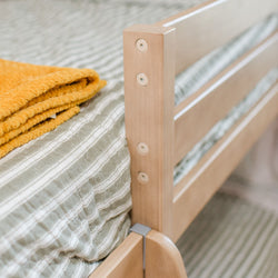 Wooden bed frame with striped bedding and folded yellow blanket.