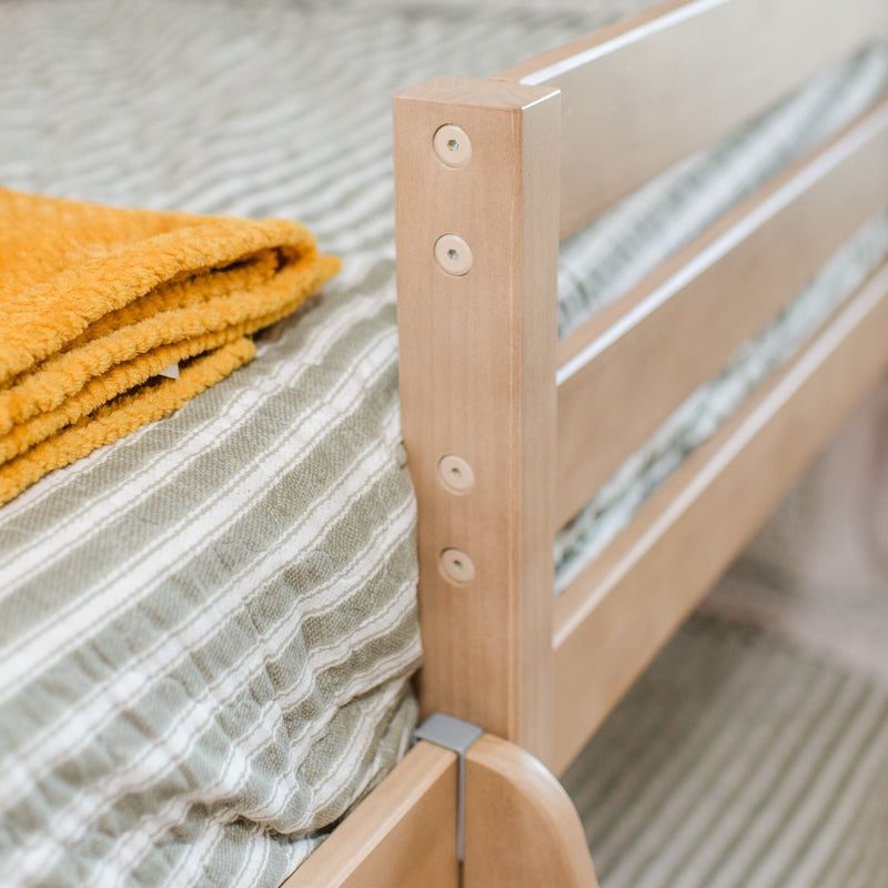 Close-up of natural wood bed frame with green striped bedding and folded mustard-yellow blanket