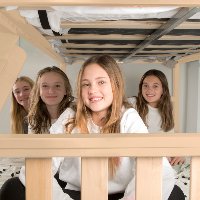 Group of friends smiling under a bed, enjoying a fun sleepover together.