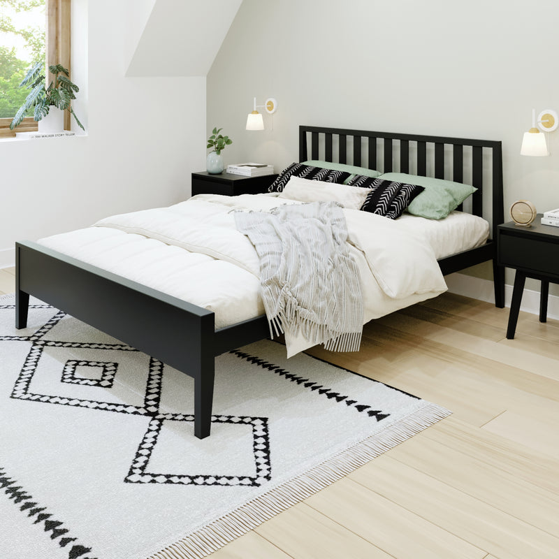 Minimalist bedroom with black slatted platform bed, white duvet and pillows, geometric black-and-white rug, light wood floor, bedside tables, wall sconces, and potted plant