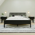 Minimalist modern bedroom with black slatted bed frame, white bedding and pillows, matching black nightstands, wall sconces, potted plant and geometric black-and-white rug