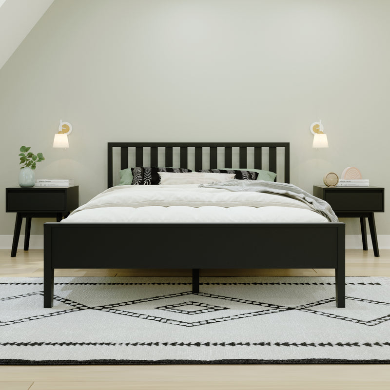 Minimalist modern bedroom with black slatted bed frame, white bedding and pillows, matching black nightstands, wall sconces, potted plant and geometric black-and-white rug