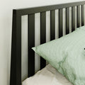 Close-up of modern black slatted metal headboard with light green pillow and textured white bedroom wall