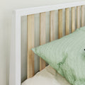 Minimalist white-framed wooden slat headboard with natural wood vertical slats and green linen pillow on a styled bed