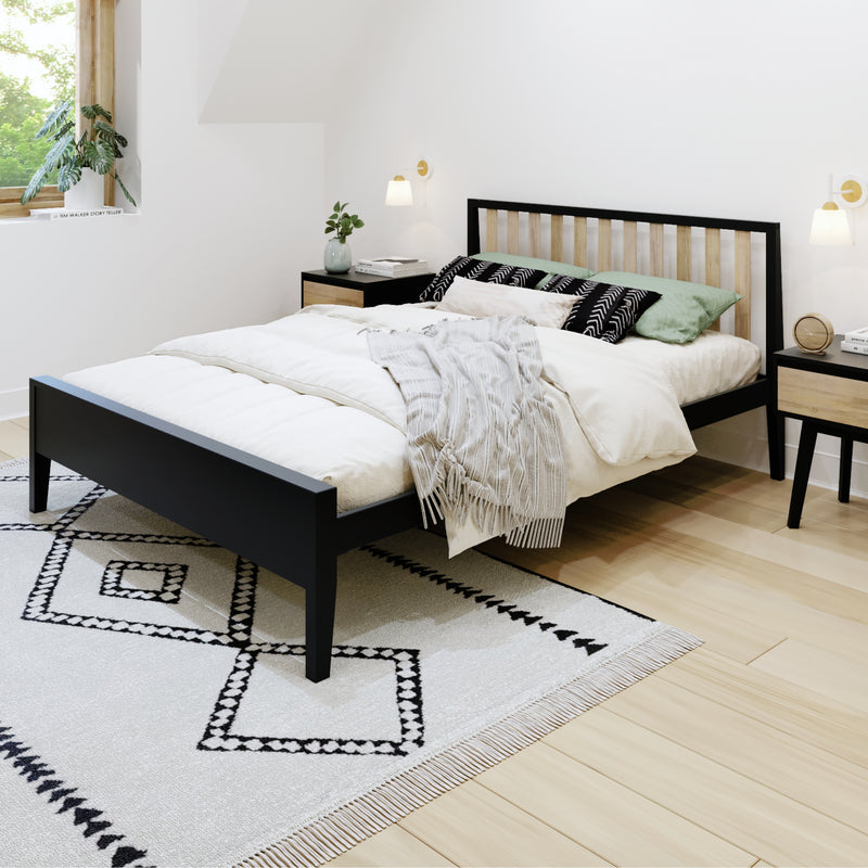 Minimalist modern bedroom with black wood bed frame and slatted headboard, white duvet and gray throw blanket, green and patterned pillows, geometric black-and-white area rug on light hardwood floor, matching nightstands, wall sconces and potted plant