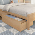 Light wood platform trundle bed with underbed storage drawers open revealing folded blankets, neutral textured quilt, blue pillows and giraffe plush toy in a cozy kids bedroom