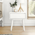 White mid-century modern nightstand with single drawer, wooden tripod lamp, potted green plant and gold-accent alarm clock on hardwood floor by window, minimalist Scandinavian bedroom decor