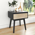 Mid-century modern black and light wood nightstand with single drawer and tapered legs, styled with lamp, clock, and plant by a window