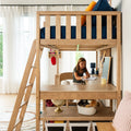 Child studying at desk beneath a natural wood loft bed in a bright modern kids' bedroom with ladder, navy bedding and storage baskets.
