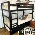 Black wooden twin-over-twin bunk bed with built-in ladder, natural wood slats, under-bed drawer, white quilted mattresses and decorative pillows in modern kids' bedroom