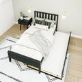 Modern minimalist bedroom with black platform bed and pull-out trundle, white bedding, black nightstand, wall sconces, light wood floor and patterned rug