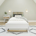 Minimalist bedroom interior with white wooden bed, green and patterned pillows, white nightstand with vase and books, and modern wall sconces on neutral walls