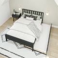 Minimalist bedroom with black wooden slatted bed frame and pull-out trundle, white bedding, green and black patterned pillows, black nightstand with plant and magazines, wall sconces, geometric rug on light hardwood floor