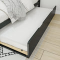 Black platform bed with white bedding and gray throw revealing a pull-out underbed trundle mattress on light hardwood floor