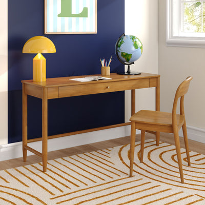 Modern wooden study desk in a bright home office with a yellow lamp, globe, pencil cup and open notebook against a navy accent wall