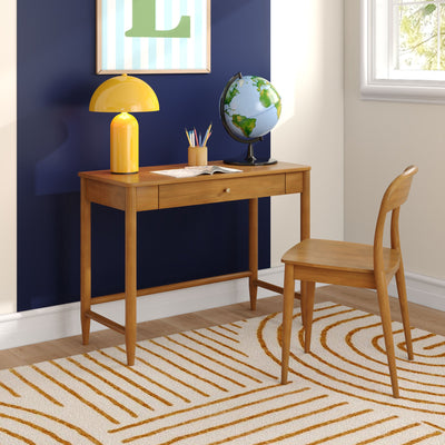 Wooden study desk with yellow lamp, globe, pencil holder and open book against a navy accent wall by a sunlit window — home office or kids study nook