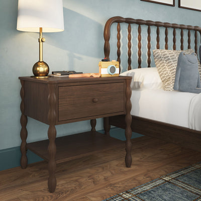 Wooden nightstand with brass lamp and toy camera beside spindle headboard bed in a cozy modern bedroom
