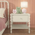 White bedside table with pink heart lamp, pink alarm clock and green frog plush next to a pastel girl's bed