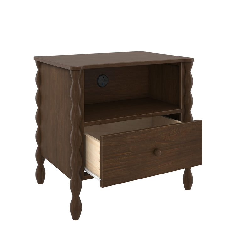 Dark brown woodgrain bedside table with single storage drawer on metal glides, open cubby shelf, built-in power outlet, and carved spindle legs