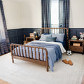 Cozy navy-and-wood kids' bedroom featuring a spindle wooden bed frame with blue quilted bedding, navy wainscoting, plaid curtains, wooden nightstands with lamp, soccer ball, slippers, rug and ukulele