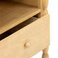 Close-up of light natural wood bedside table with open drawer, round wooden knob and turned leg