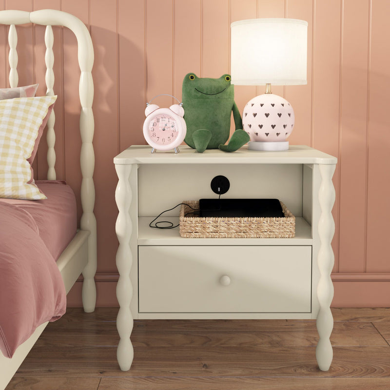 Kids white nightstand with pink heart lamp, green stuffed frog, pink alarm clock and wicker basket holding a charging tablet in blush bedroom.