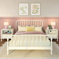 Cozy pastel bedroom featuring a white spindle bed with yellow gingham bedding, pink scalloped wainscoting, matching white nightstands with lamps and decor, framed floral prints and woven jute rug