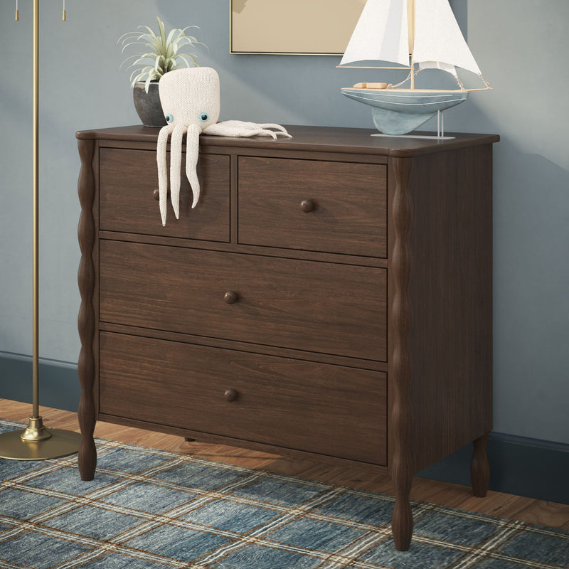 Dark walnut four-drawer dresser with carved legs in coastal nursery setting, styled with knitted octopus toy, potted plant, toy sailboat and blue plaid rug