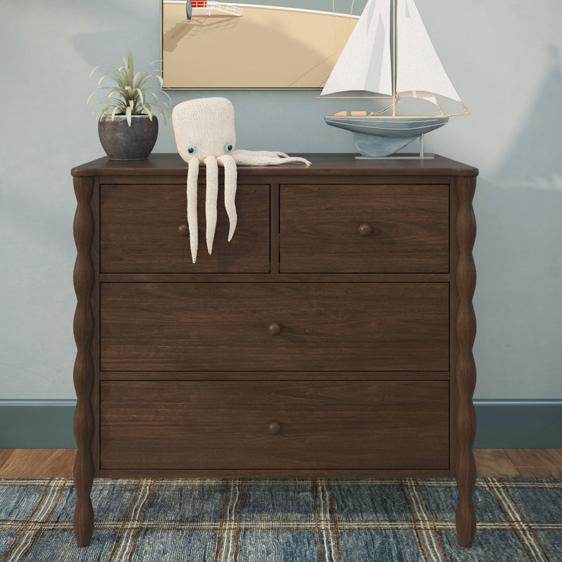 Walnut three-drawer nursery dresser with carved scalloped legs styled with knitted octopus toy, model sailboat, potted plant and coastal wall art on blue area rug