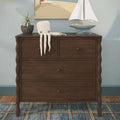 Dark wood dresser styled with knitted octopus toy draped over edge, blue model sailboat, potted plant and coastal nursery decor wall art