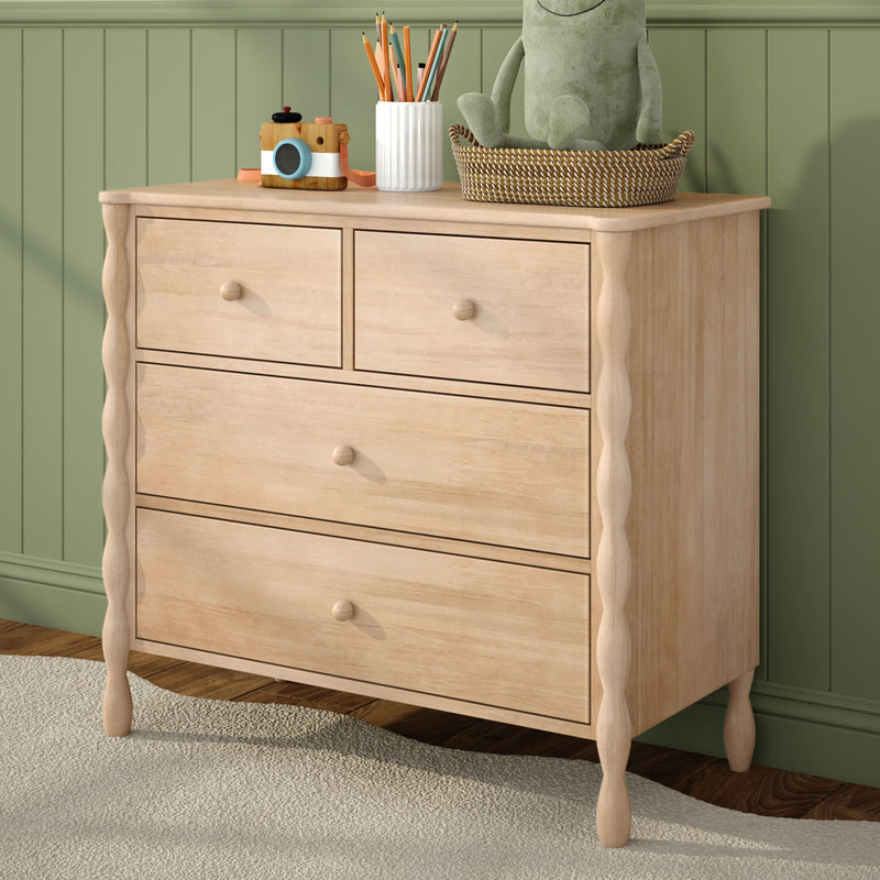 Light wood dresser in kids' room with green paneled wall, wooden toy camera, white pencil cup, woven basket and plush frog