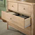 Light natural wood dresser with turned legs and an open drawer revealing folded clothes, bedroom storage chest