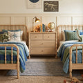 Kids twin bedroom with light wooden spindle beds, blue-green quilts, bedside dresser with brass lamp and globe, nautical compass pillow and dinosaur toys