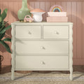 Nursery dresser decor with pastel kids room accessories: wooden toys and rainbow stacker, mushroom-shaped lamp, pink toy car, green vase and stacked storage boxes on cream dresser