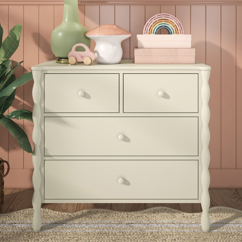 Nursery dresser decor with pastel kids room accessories: wooden toys and rainbow stacker, mushroom-shaped lamp, pink toy car, green vase and stacked storage boxes on cream dresser