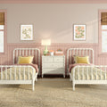 Pastel pink twin girls bedroom nursery with white spindle twin beds, yellow gingham bedding, white nightstand and lamp, scalloped wainscoting and floral wall art