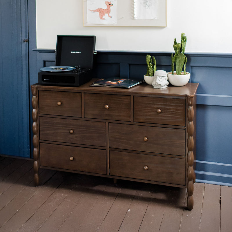 Brown six-drawer wooden dresser topped with a record player, open vinyl, potted cacti and decorative Stormtrooper helmet against blue wainscoting.