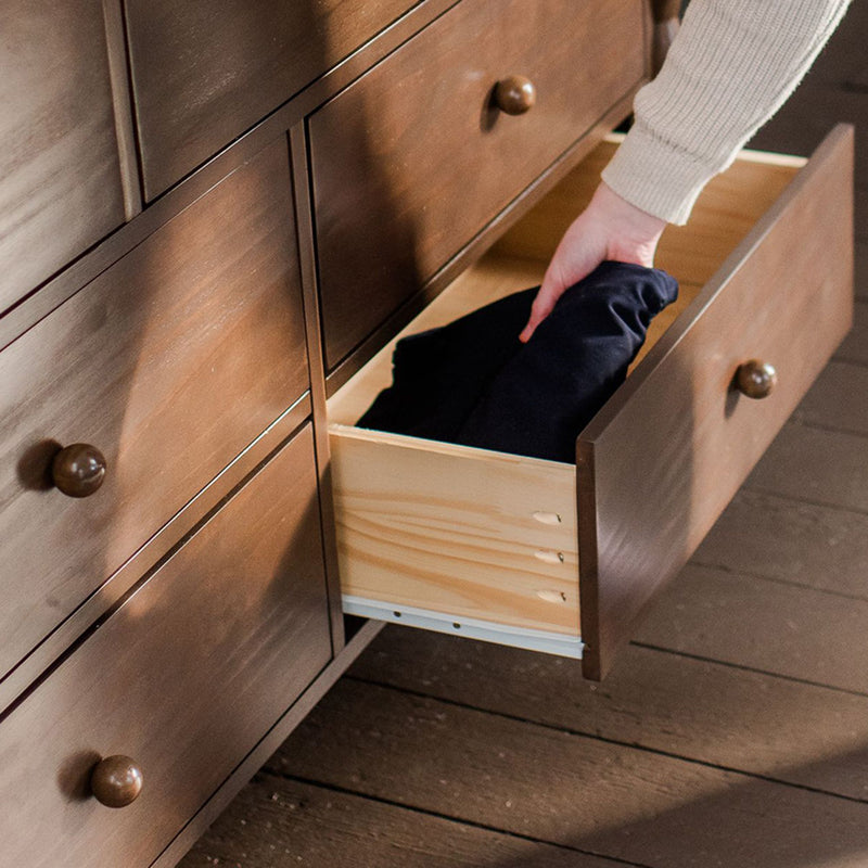 Hand placing folded clothes into open wooden dresser drawer — bedroom storage and organization