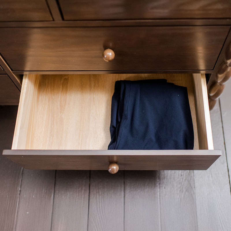 Open dark wood dresser drawer containing neatly folded black pants on light wood interior, bedroom storage and organization