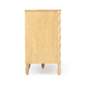Side view of light wood chest of drawers with natural finish, turned legs and carved scalloped front edge.