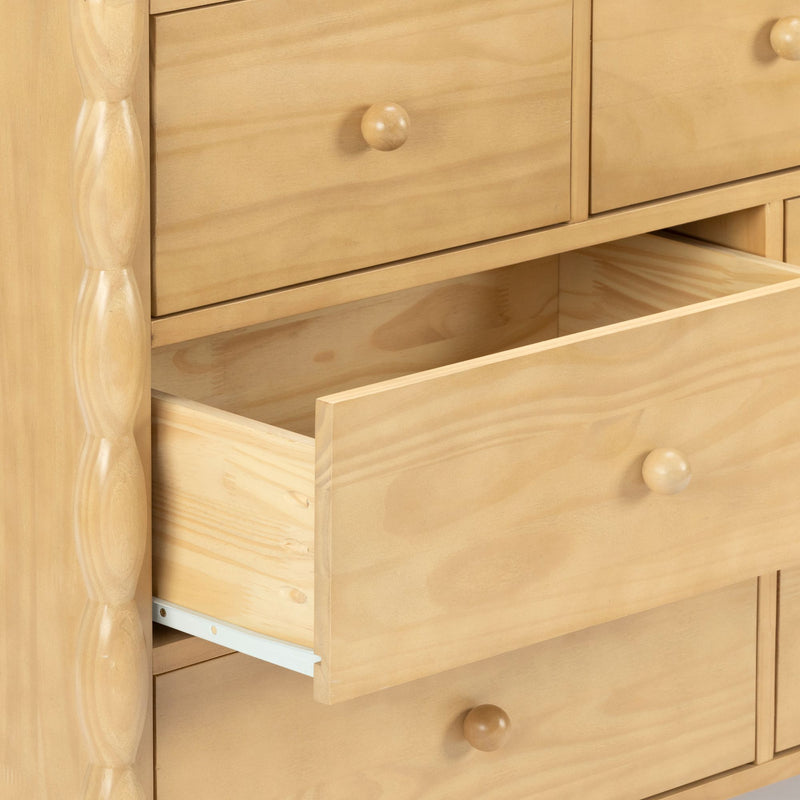Close-up of light pine wood chest of drawers with one open drawer and round wooden knobs, natural finish bedroom storage furniture