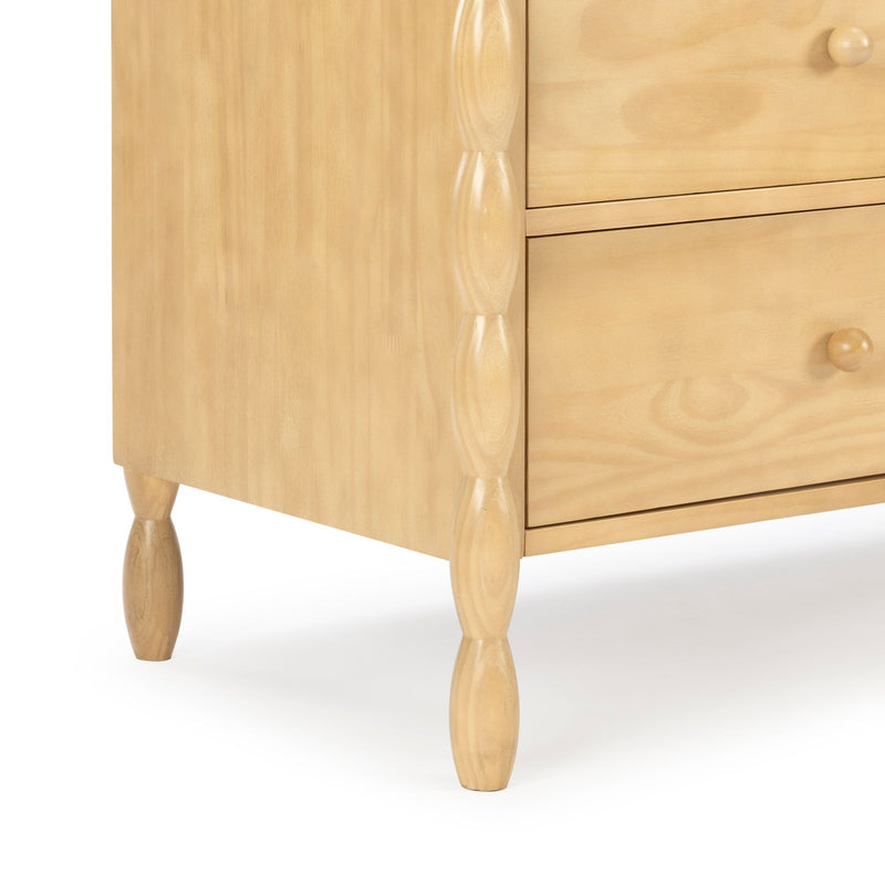 Close-up of light natural wood dresser corner with turned spindle legs and two knobbed drawers, Scandinavian-style bedroom furniture