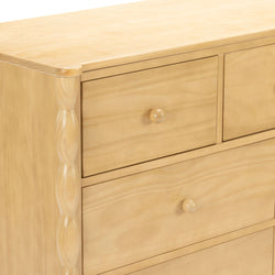 Close-up of light wood dresser drawers with round wooden knobs and carved side trim, pine-finish bedroom chest