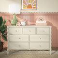 Cream wooden nursery dresser in children's room with green table lamp, mushroom and wooden car toys, pastel rainbow decor, pink scalloped wainscoting and potted plant