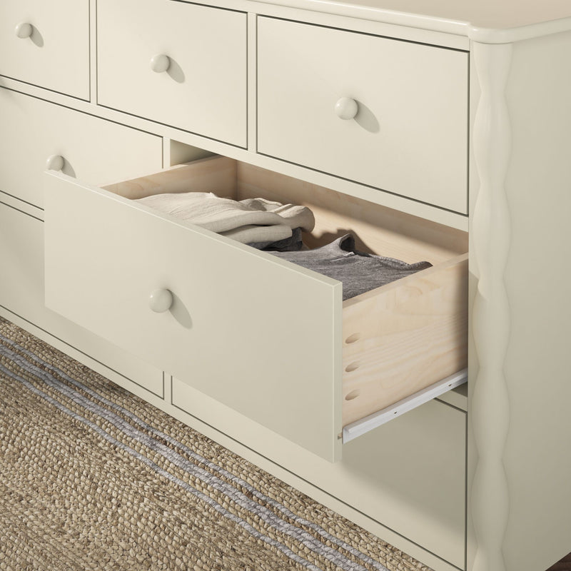 Cream wooden dresser with open drawer showing folded neutral clothing and natural wood drawer interior on woven jute rug, bedroom storage furniture