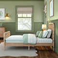 Green children's bedroom with wooden twin bed, mint-and-white nature-themed bedding, stuffed toys, window with Roman shade, lamp and wooden dresser